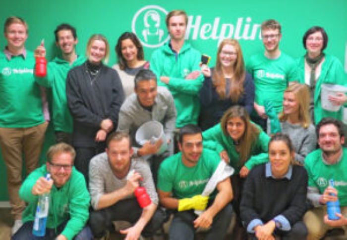 Gruppe von Menschen in grünen Helpling-Shirts mit Reinigungsutensilien, lächelnd.