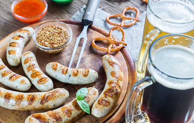 Bratwürste auf Holzplatte mit Senf, Brezeln und Bierkrügen. Perfekt für die Reinigungskraft-Pause.