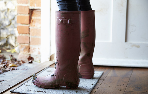 Schmutzige Gummistiefel auf Fußmatte vor weißer Tür, geeignet für reinigung.