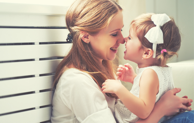 Mutter und Kind lächeln sich an, sitzen nah zusammen, helle Umgebung.