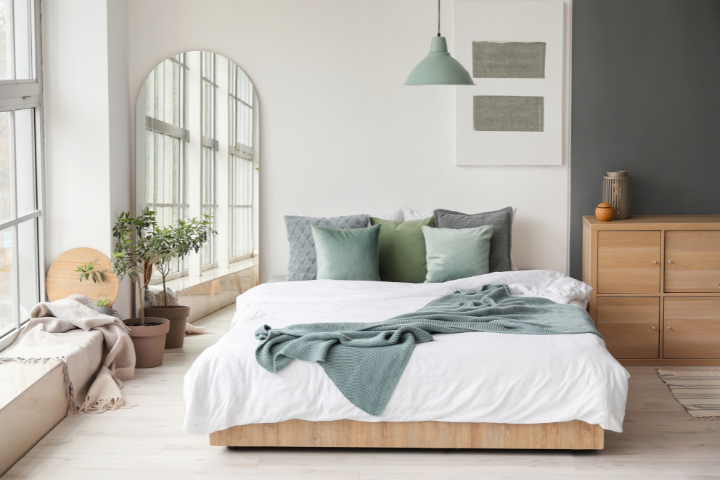 Helles Schlafzimmer mit Bett, Pflanzen, Spiegel und Kommode; ideal zum Reinigen und Aufräumen.