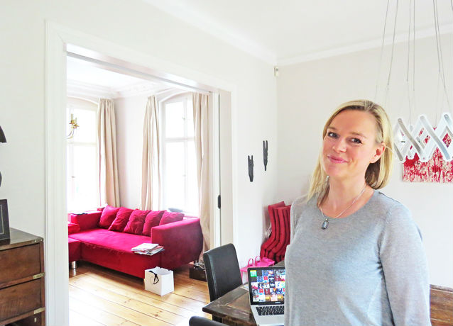 Frau in hellem Raum mit rotem Sofa, Laptop auf Tisch; Thema: Reinigungskraft.