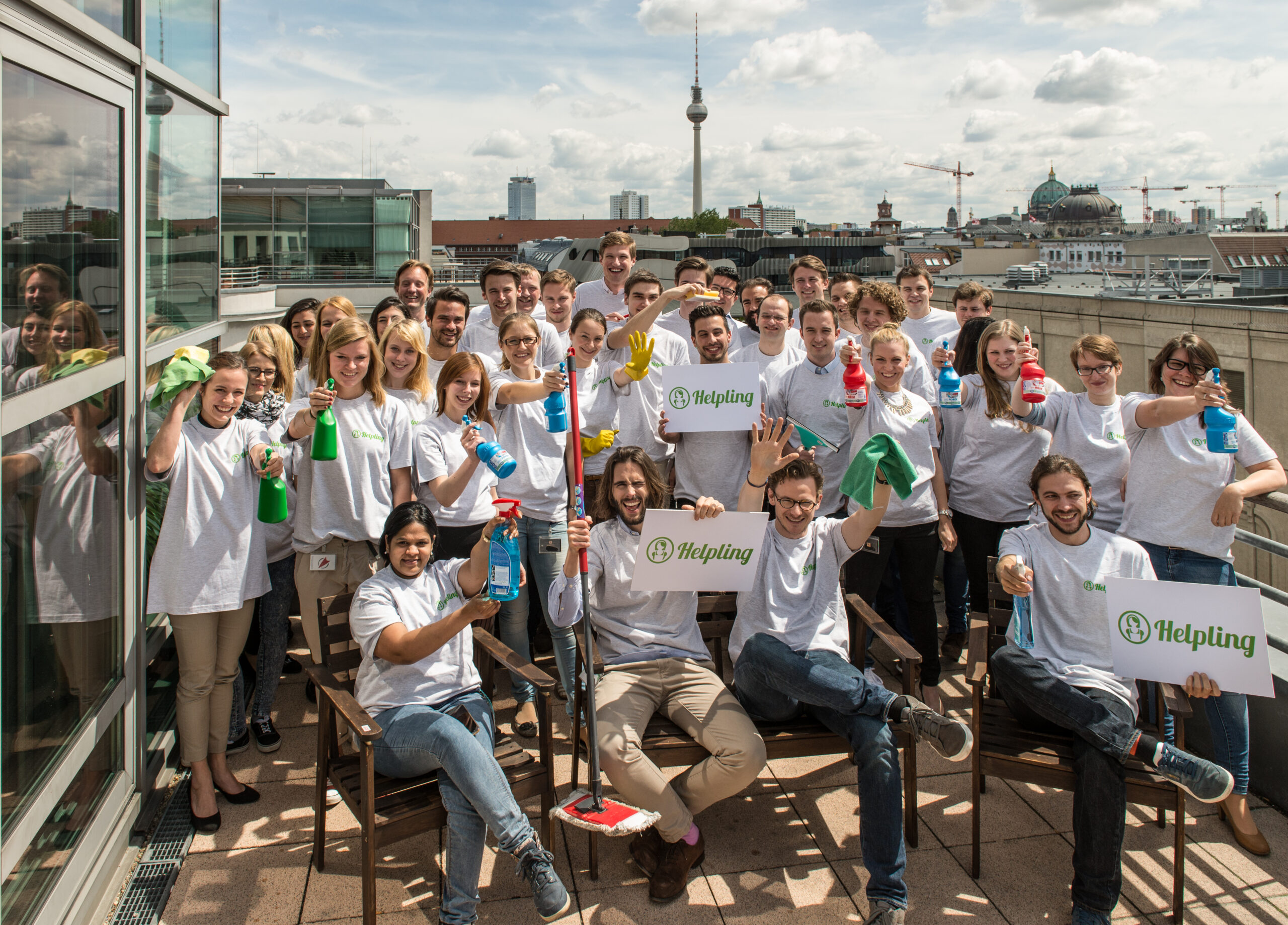 Gruppe von Menschen mit Reinigungsprodukten und Helpling-Logos auf einer Dachterrasse.