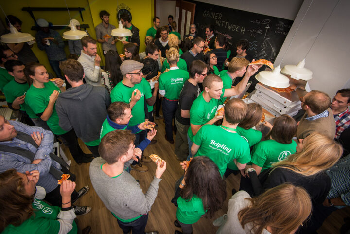 Menschen in grünen Shirts essen Pizza bei einer Veranstaltung, Thema Reinigung.