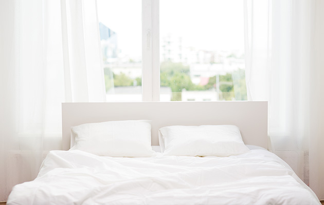 Helles Schlafzimmer mit weißem Bett vor großen Fenstern, ideal für eine Putzfrau zu reinigen.