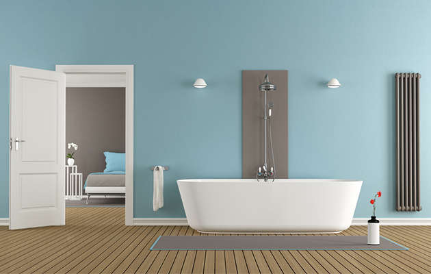 Modernes Badezimmer mit freistehender Badewanne, blauer Wand und geöffneter Tür zum Schlafzimmer.