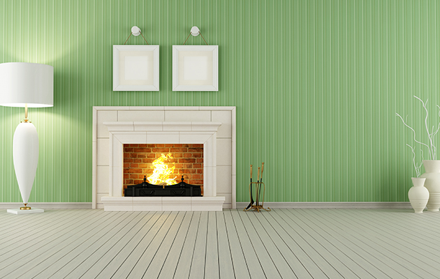 Grünes Wohnzimmer mit Kamin, zwei Bilderrahmen, Stehlampe und Vasen. Reinigung notwendig.