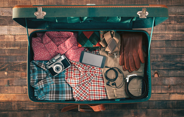 Offener Koffer mit Kleidung, Kamera, Smartphone und Kopfhörern auf Holzboden; Thema Reisen.