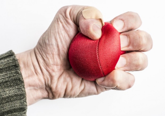 Hand mit Pflaster drückt roten Stressball, geeignet für Putzfrau zur Entspannung.