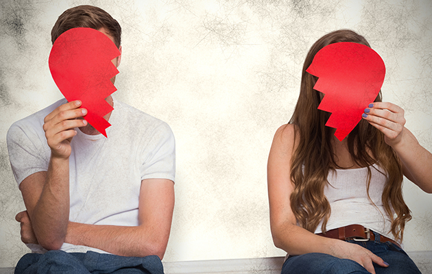 Zwei Personen halten gebrochene Herzen aus Papier vor ihre Gesichter, Symbol für Trennung.