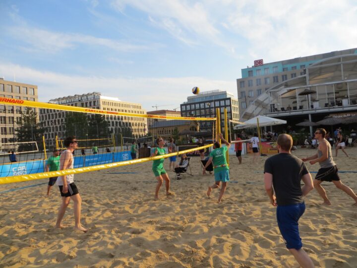 Menschen spielen Beachvolleyball auf einem Sandplatz in der Stadt bei sonnigem Wetter.