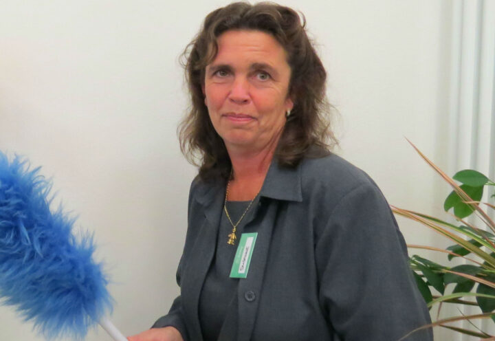 Frau mit Staubwedel, Namensschild, Pflanzen im Hintergrund, reinigungskraft.