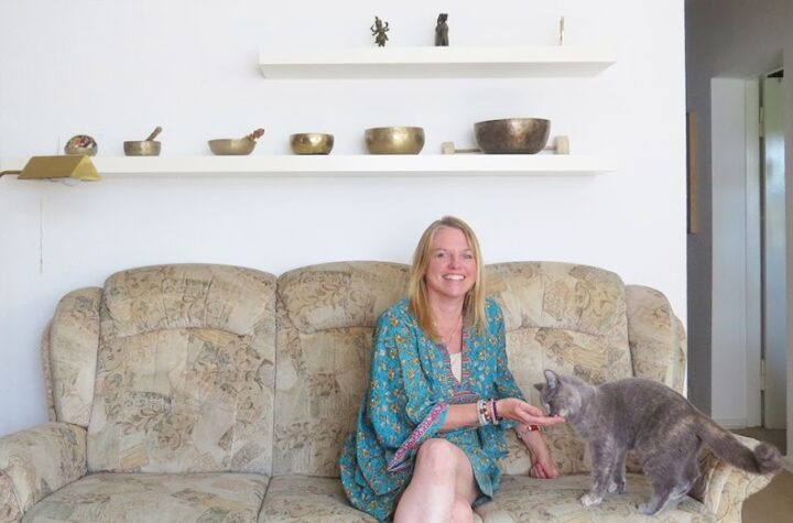 Frau auf Sofa mit Katze, tibetische Klangschalen im Hintergrund, reinigungskraft.