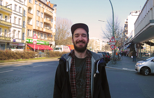 Lächelnder Mann mit Kappe auf Stadtstraße, Gebäude im Hintergrund, reinigungskraft.