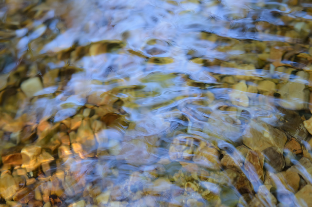 Fließendes Wasser über bunten Steinen, klare Details, ähnlich wie bei einer gründlichen Reinigung.