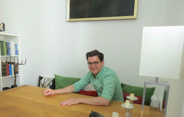 Mann am Tisch mit Kerzenhalter, Bücherregal im Hintergrund; Thema: reinigungskraft.