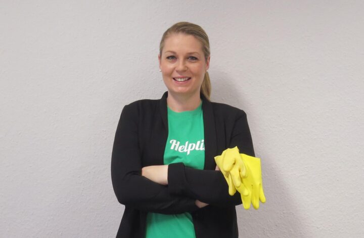 Frau mit gelbem Handschuh, grünem T-Shirt und schwarzem Blazer, lächelnd; Reinigungskraft.