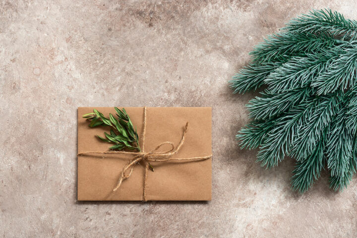 Braunes Geschenk mit Zweig, daneben Tannenzweige, auf Steinboden. Reinigen erforderlich.