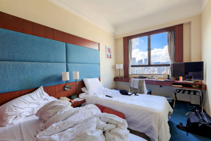 Unordentliches Hotelzimmer mit zwei Betten, Stadtblick und Reinigungsbedarf.