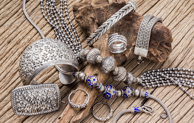 Silberschmuck auf Holz, darunter Armbänder, Ringe und Halsketten, die eine Reinigung benötigen.