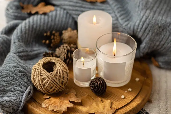Kerzen auf Holztablett mit Zapfen, Blättern und Garnknäuel, umgeben von grauem Stoff.