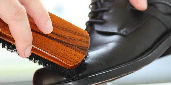 Schwarzer Lederschuh wird mit Holzbürste poliert, reinigungskraft im Einsatz.
