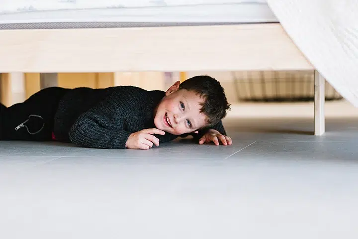 Kind lächelt fröhlich unter einem Bett auf einem sauberen Boden, ideal für eine Putzfrau.