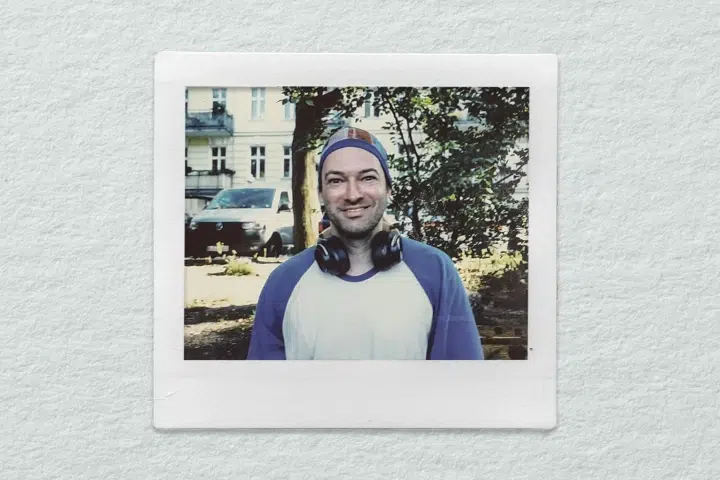 Person mit Kopfhörern im Freien, lächelnd, im Hintergrund Gebäude und Auto, reinigung.