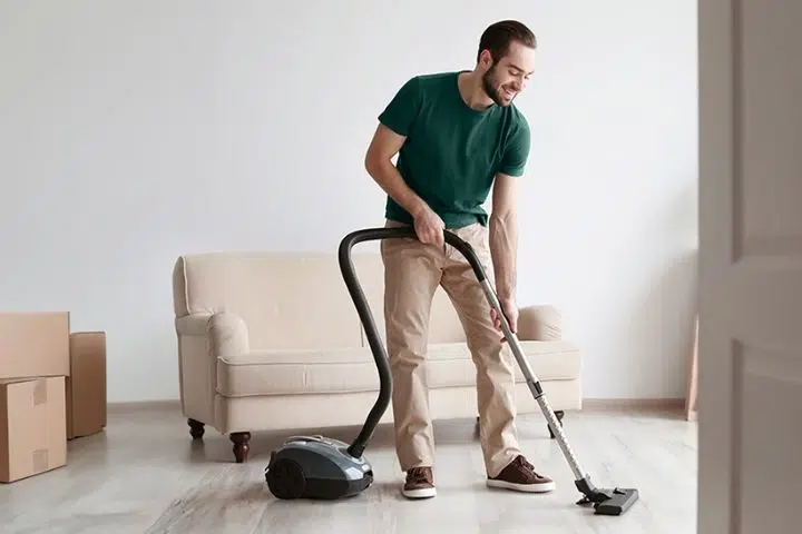Mann beim Staubsaugen im Wohnzimmer, Kartons im Hintergrund, reinigung.
