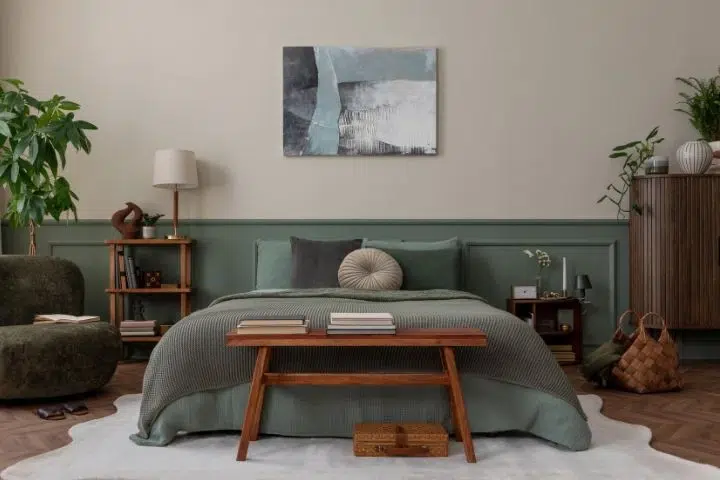 Schlafzimmer mit grünem Bett, Holzmöbeln, Pflanzen und abstraktem Gemälde. Reinigungskraft.