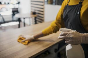 Side View Female Barista Cleaning Table While Wearing Latex Gloves