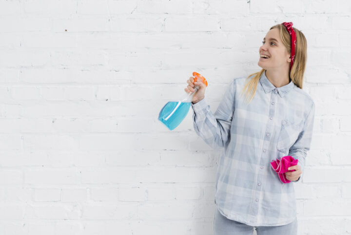 Frau mit Sprühflasche und Tuch vor weißer Wand, lächelnd, reinigungskraft.