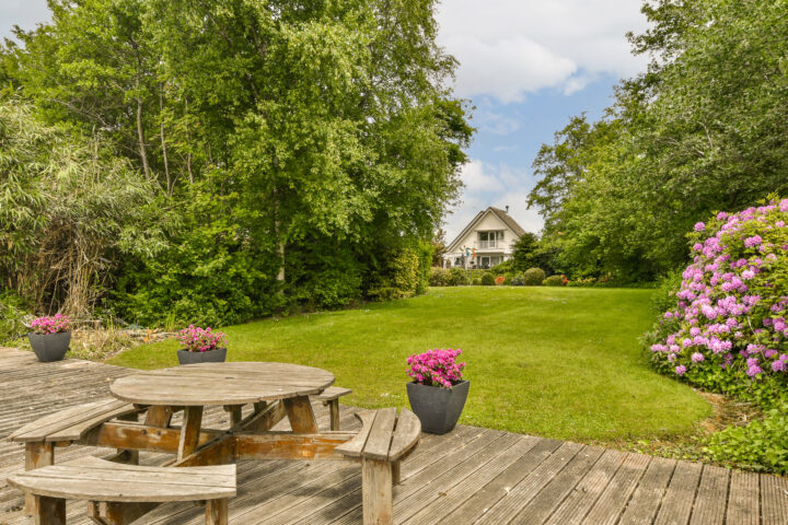 Holztisch auf Terrasse, Blumen, Rasen, Bäume, Haus im Hintergrund, ideal für reinigung.