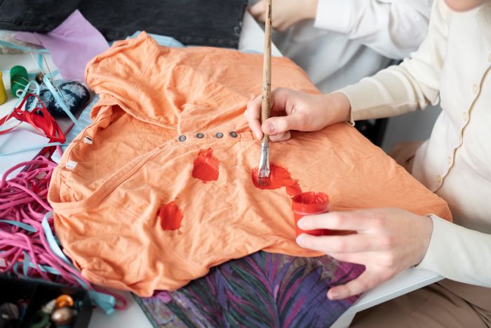 Person Bemalt Orangefarbenes Hemd Mit Roter Farbe, Um Flecken Zu Verdecken. Reinigungskraft.