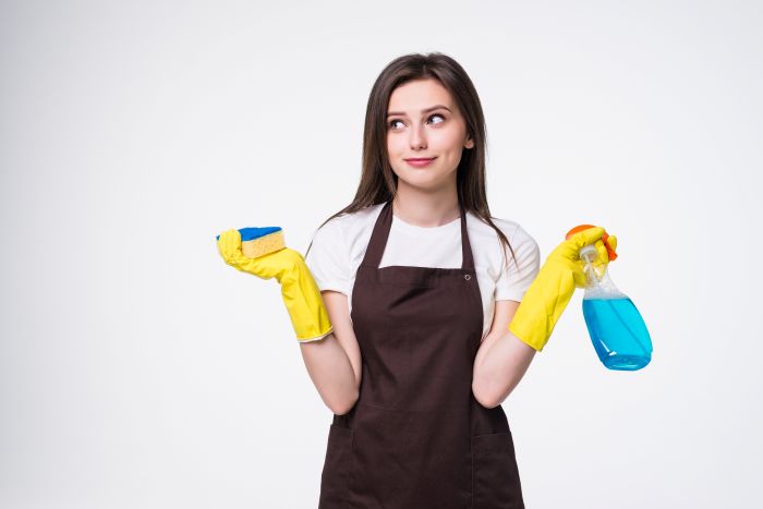 Frau mit gelben Handschuhen hält Schwamm und Reinigungsmittel. Thema: Reinigungskraft.