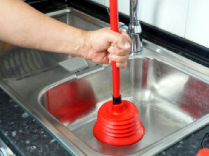 Hand benutzt roten Pümpel in Edelstahlspüle zum Reinigen und Entstopfen.