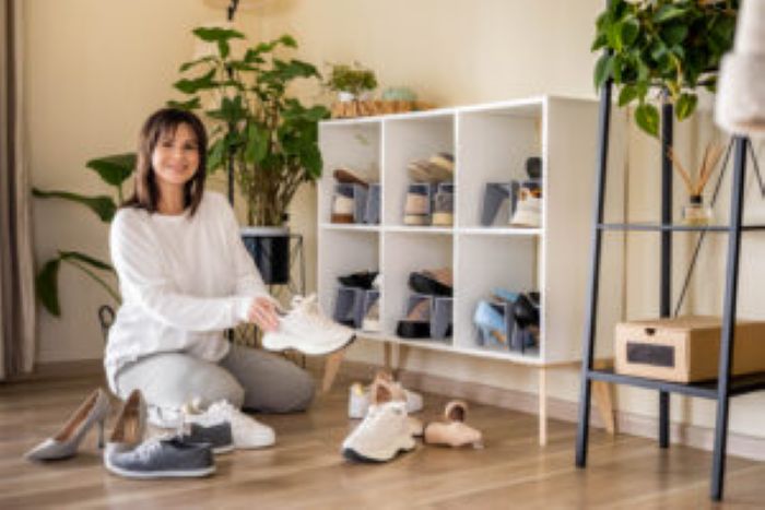 Frau ordnet Schuhe vor Regal, Pflanzen im Hintergrund, reinigungskraft im gemütlichen Raum.