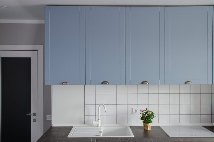 Blaue Küchenschränke, weiße Fliesen, Spüle, Pflanze; ideal für Reinigung und Putzfrau.