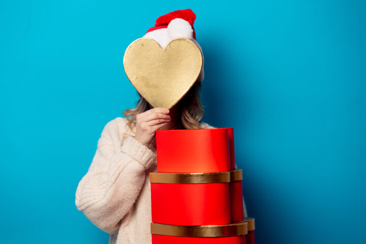 Person mit Weihnachtsmütze hält goldenes Herz und rote Geschenkboxen, reinigung.