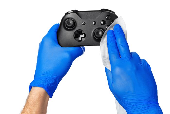 Blaue Handschuhe reinigen Gamecontroller mit Tuch; Reinigungskraft im Einsatz.