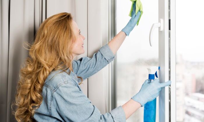 Frau reinigt Fenster mit Tuch und Spray, trägt Handschuhe, Putzfrau bei der Arbeit.