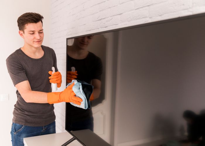 Mann mit Handschuhen reinigt Fernseher mit Tuch und Spray, reinigungskraft.