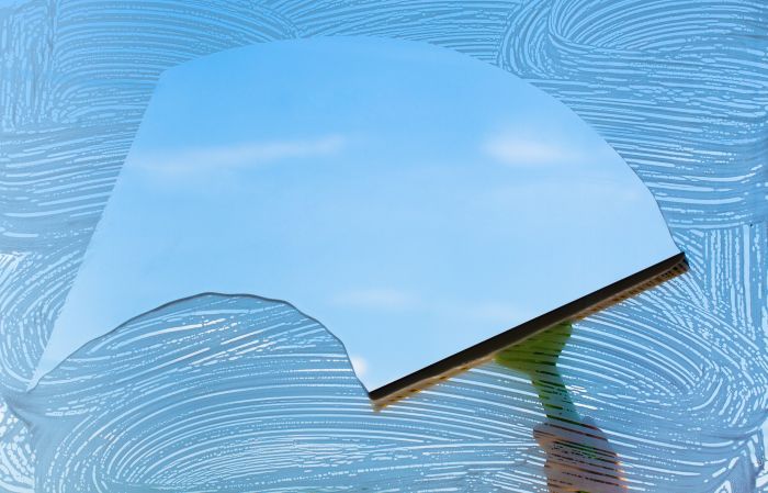 Fensterabzieher reinigt Glas, klare Sicht auf blauen Himmel, Thema: putzen.