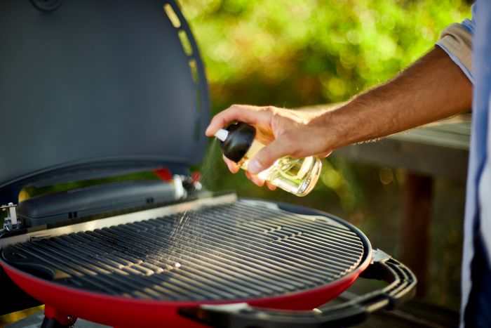 Hand sprüht Flüssigkeit auf Grillrost im Freien, Reinigung des Grills.