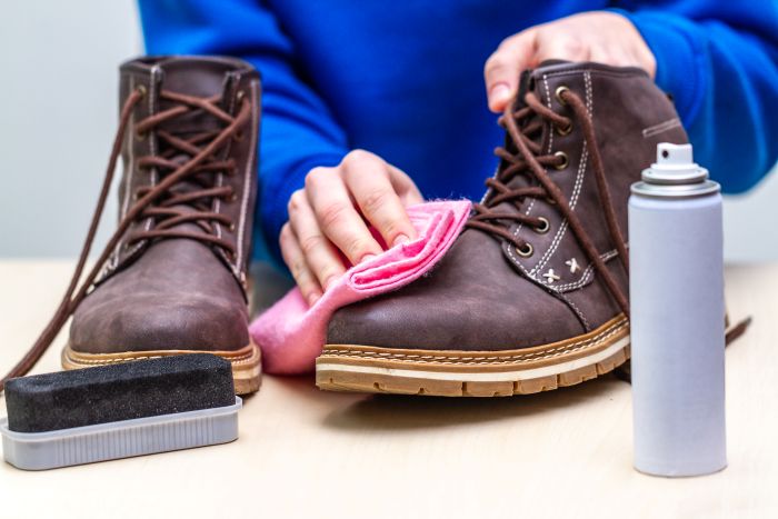 Braune Stiefel werden mit Tuch, Bürste und Spray gereinigt; Fokus auf Schuhpflege.
