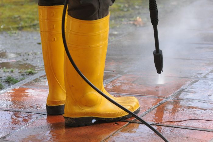 Person Wearing Yellow Rubber Boots With High Pressure Water Nozzle Cleaning Dirt Tiles 1