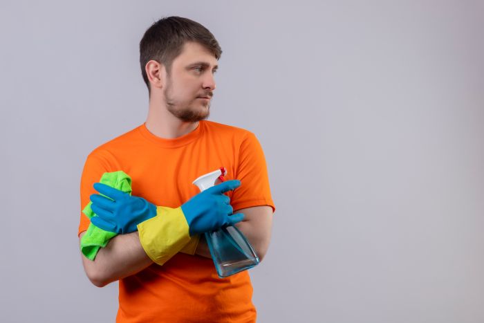 Young Man Wearing Orange T Shirt Rubber Gloves Holding Cleaning Spray Rug Standing With Arms Crossed
