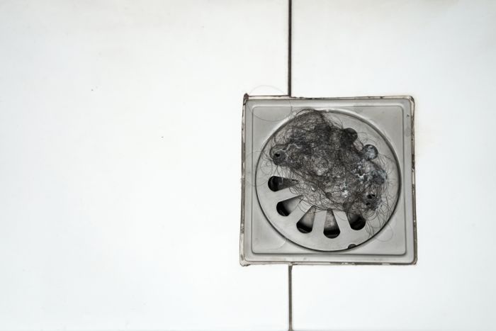 Abfluss mit Haaren verstopft, erfordert Reinigung durch Putzfrau oder Reinigungskraft.