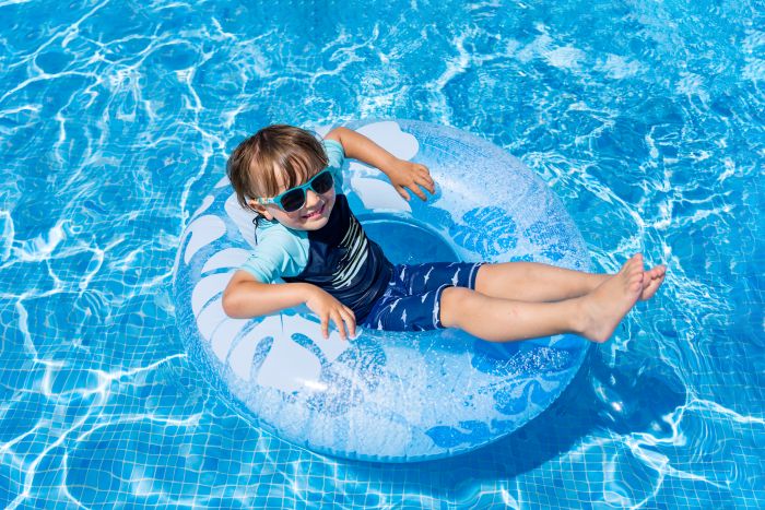 Kind mit Sonnenbrille auf Schwimmring im Pool; Wasser sauber wie von Putzfrau gereinigt.