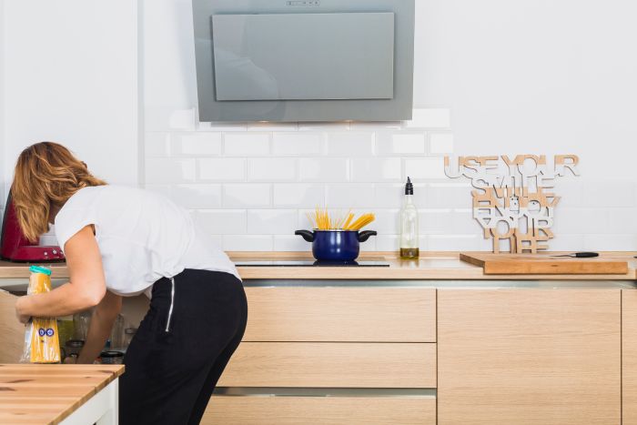 Woman Bending Down Putting Food Cabinet